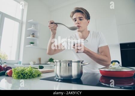 Portrait of his he nice attractive cute puzzled focused guy making dinner lunch luncheon boiling soup at light white modern style interior house Stock Photo