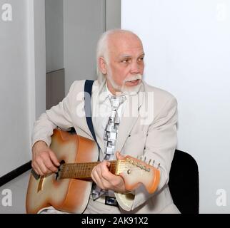 Portrait of senior grey bearded bald man in light business suit that is sitting with guitar in office interior. Stock Photo