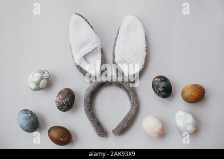 Stylish easter eggs and bunny ears flat lay on gray wallpaper with copy space. Natural dyed colorful easter eggs and grey rabbit ears. Seasons greetin Stock Photo