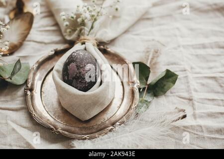 Rustic Easter table decorations. Stylish Easter brunch table setting with egg in easter bunny napkin. Modern natural dyed marble egg on napkin with bu Stock Photo