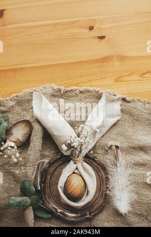 Rustic Easter table decorations. Stylish Easter brunch table setting with egg in easter bunny napkin. Modern natural dyed green egg on napkin with bun Stock Photo