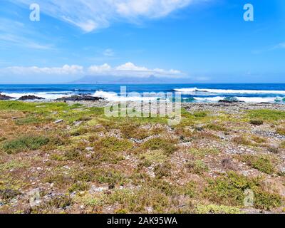 Down the rocky shore of Robben Island to a distant Cape Town. Stock Photo
