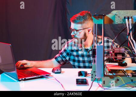 Technology and engineering concept - Male engineer working at night in the lab, he is adjusting a 3D printer components Stock Photo