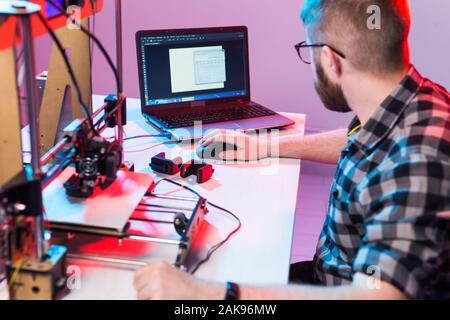 Technology and engineering concept - Male engineer working at night in the lab, he is adjusting a 3D printer components Stock Photo