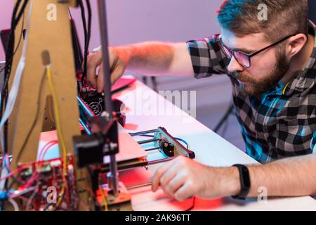Technology and engineering concept - Male engineer working at night in the lab, he is adjusting a 3D printer components Stock Photo