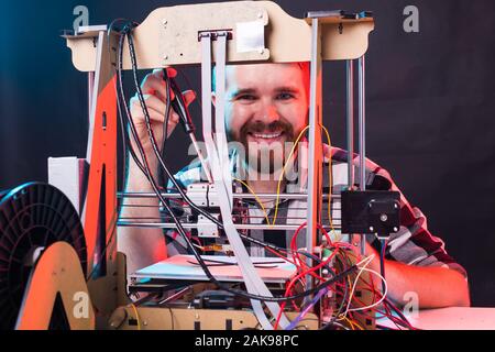Technology and engineering concept - Male engineer working at night in the lab, he is adjusting a 3D printer components Stock Photo