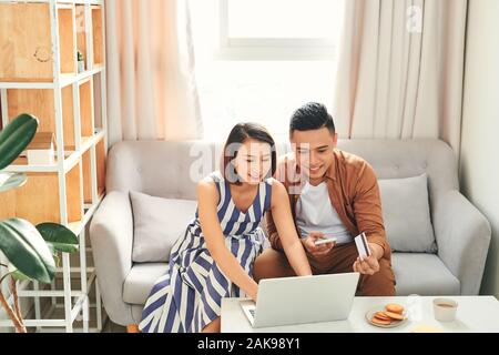 Young Asian couple paying bills by laptop with credit card at home Stock Photo