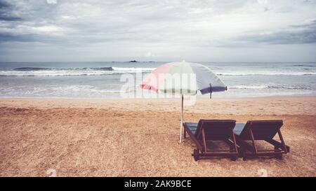 Two sunbeds and umbrella on an empty beach, color toning applied, Sri Lanka. Stock Photo