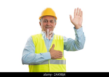 Old male builder smiling as making honest oath touching chest and holding hand up isolated on white Stock Photo