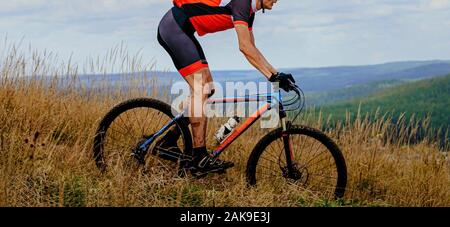 male cyclist downhill rides trail in dry grass. mud on feet and mountain bike Stock Photo