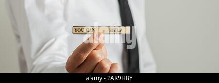 Wide view image of businessman holding a paper with You can help sign in a conceptual image. Closeup view. Stock Photo