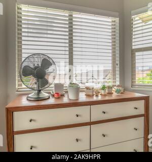 Square Potted cacti and electric fan on wooden cabinet against bay window of a home Stock Photo