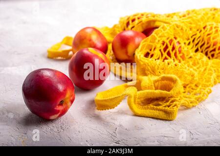 Nectarines in yellow string mesh reusable bag on the table Stock Photo
