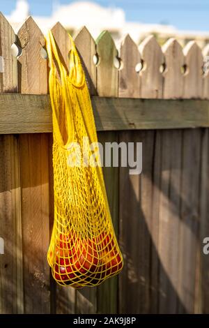 Nectarines in yellow string mesh reusable bag on the fence Stock Photo
