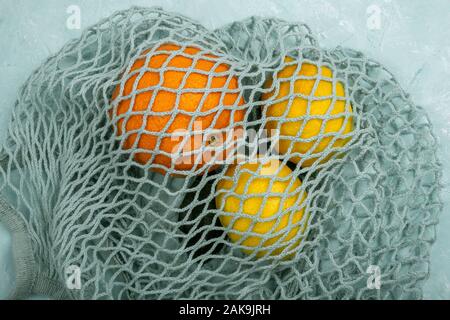 Lemons and orange in blue string mesh reusable bag on the table Stock Photo