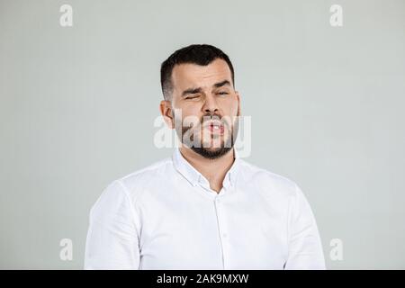 Portrait of young frowned handsome bearded man on gray background. facial expression. man grimaced Stock Photo
