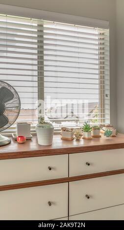 Vertical frame Potted cacti and electric fan on wooden cabinet against bay window of a home Stock Photo