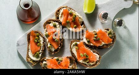 rye bread sandwiches with smoked salmon and capers on a marble board and sesame oil with slices of lime Stock Photo