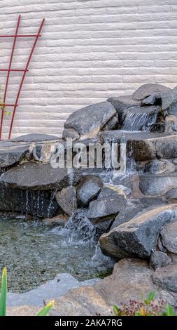Vertical Artificial stone cascade waterfall in backyard on a sunny day Stock Photo