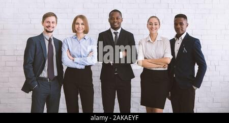 Confident team. Successful colleagues posing at camera, white brick wall background, panorama Stock Photo