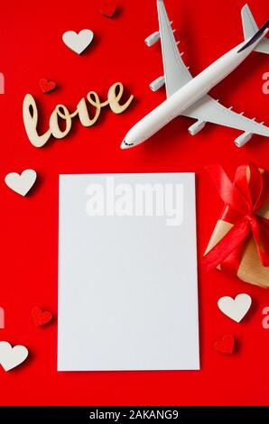 Travel planning on Valentines day . Travel concept, mockup. Blank white paper, model of passenger plane, gift box and inscription love on red backgrou Stock Photo