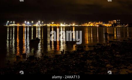 Night time colour photograph looking over open water with Poole harbour brightly lit in background, taken in Poole, Dorset, England. Stock Photo