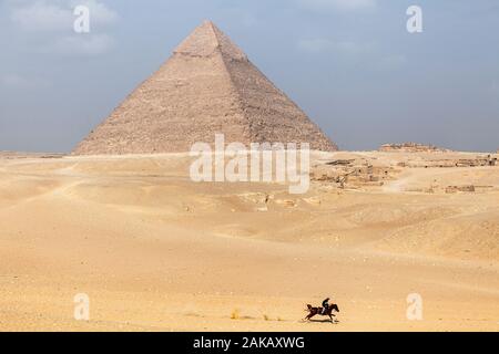 A man rides a horse  through the desert sand on Giza Plateau near the Great Pyramids of Egypt Stock Photo