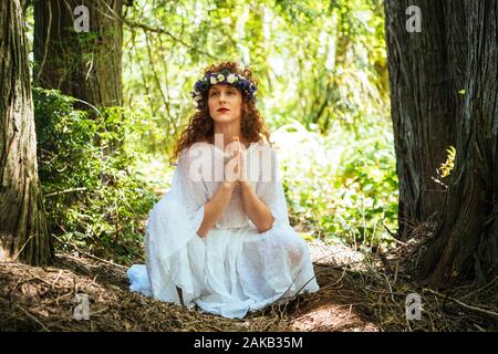 Woman with flower sitting with hands clasped in forest,  Bainbridge Island, Washington State, USA Stock Photo