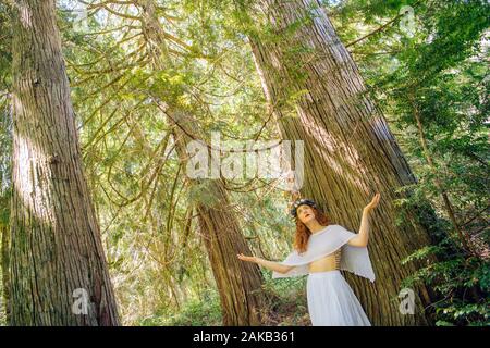 Woman with flower standing in forest,  Bainbridge Island, Washington State, USA Stock Photo
