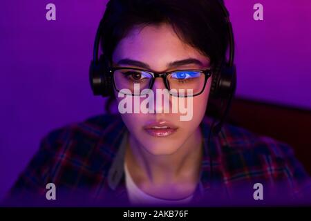 Female programmer working on laptop late at night. Room illuminated by neon light Stock Photo