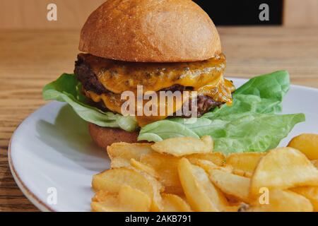 Double beef burger with double cheese and salad. Served with potato dippers on the white plate. American cuisine closeup. Stock Photo