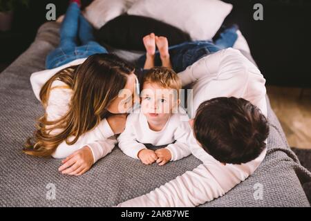 Happy family having fun lying down on bed at home. Happy Family In Bed. Mom dad and son lie on bedroom at within doors. father, mother and child Stock Photo
