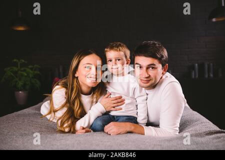 Parents with their baby boy on bed at home. Families with child in bed at night at home. Happy family enjoying in bed. Mom, dad and kid play in the Stock Photo