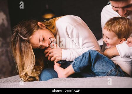 Parents with their baby boy on bed at home. Families with child in bed at night at home. Happy family enjoying in bed. Mom, dad and kid play in the Stock Photo