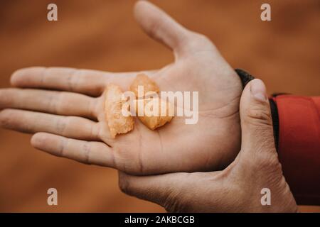 two hands holding and showing pieces of red quartz sandstone Stock Photo