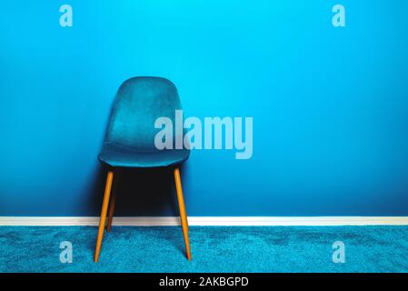 Modern Blue Velour Chair on wooden legs, blue background Stock Photo