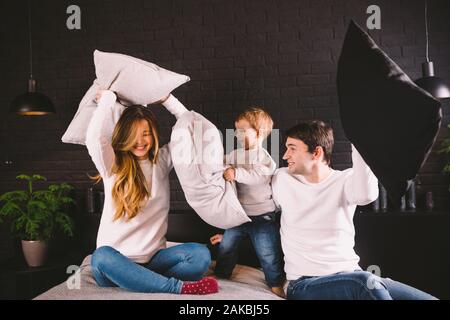 Family having funny pillow fight on bed. Parents spending free time with their son. Young family being playful at home. Happy parents and child. Young Stock Photo