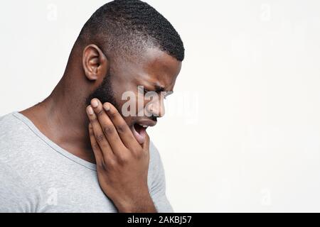 Young afro man having acute toothache, holding his jaw, copy space Stock Photo