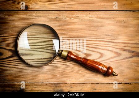 A magnifying glass on a wooden table in a close up view Stock Photo
