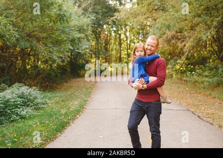 A smiling father holds small daughter in his arms on a tree-lined path Stock Photo