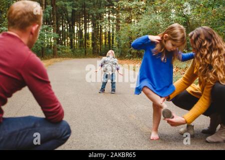 A mother helps her child with a shoe while a toddler throws a tantrum Stock Photo