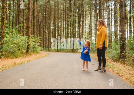 A small child stands on a wooded path with her mother pointing up Stock Photo