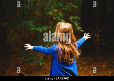 A small girl throws out arms to embrace the dark woods in front of her Stock Photo