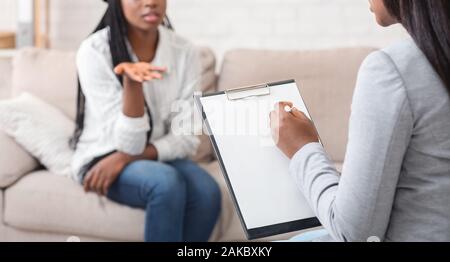 Psychologist having therapy session with her patient in office, listening problems of young woman and taking notes, panorama Stock Photo