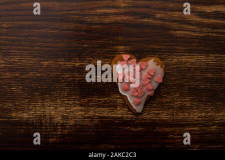 one homemade heart-shaped gingerbread with white icing and colorful sugar decoration on the background of an old wooden table Stock Photo