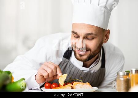Cooking Fish. Professional Chef Guy Plating Salmon Dish Preparing Dinner Standing In Restaurant Kitchen. Selective Focus Stock Photo