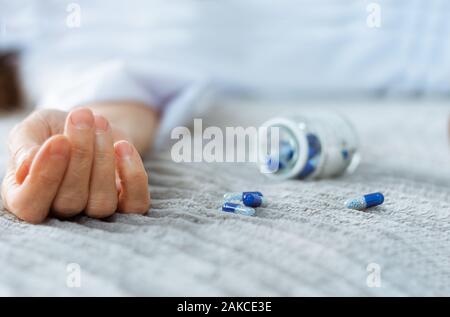 Woman’s hand close up committing suicide by overdosing on medication, pills and bottle beside. Overdose pills and addict concept background Stock Photo