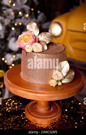 Chocolate cake with raspberry filling and pistachio cream, decorated with roses and golden jelly sparkles in the New Year's interior Stock Photo