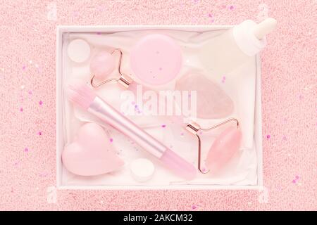 beauty box with rose quartz jade roller and massage stone, face serum and mask brush on pastel pink background Stock Photo