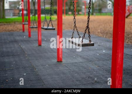 A set of children's swings in a park with the focus on the swing closest to camera Stock Photo